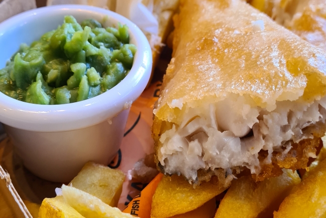 Close up of a piece of battered fish and mushy peas.